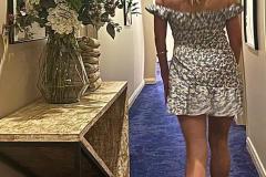 Chrissie walking down a blue-carpeted corridor wearing a floral dress.